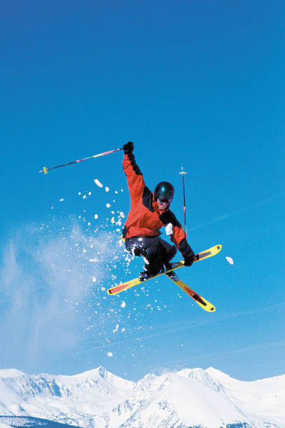 A skier mid-air performing a trick against a bright blue sky, snow flying.